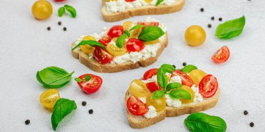 Domates kirazlı, krem peynirli ve fesleğenli taze ekmek sandviçleri. Sabah kahvaltısı kavramı. Sert ışık, koyu gölge, beyaz taş zemin, afiş biçimi