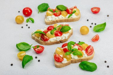 Domates kirazlı, krem peynirli ve fesleğenli taze ekmek sandviçleri. Sabah kahvaltısı kavramı. Sert ışık, karanlık gölge, beyaz taş beton arka plan, kapat