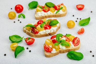 Domates kirazlı, krem peynirli ve fesleğenli taze ekmek sandviçleri. Sabah kahvaltısı kavramı. Sert ışık, karanlık gölge, beyaz taş beton arka plan, kapat