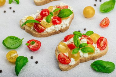 Domates kirazlı, krem peynirli ve fesleğenli taze ekmek sandviçleri. Sabah kahvaltısı kavramı. Sert ışık, karanlık gölge, beyaz taş beton arka plan, kapat