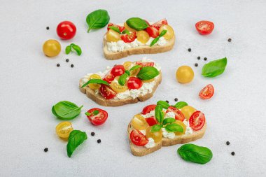Domates kirazlı, krem peynirli ve fesleğenli taze ekmek sandviçleri. Sabah kahvaltısı kavramı. Sert ışık, karanlık gölge, beyaz taş zemin, kopyalama alanı
