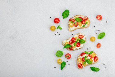 Domates kirazlı, krem peynirli ve fesleğenli taze ekmek sandviçleri. Sabah kahvaltısı kavramı. Sert ışık, karanlık gölge, beyaz taş arka plan, üst görüş