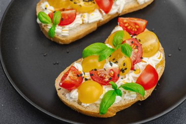 Domates kirazlı, krem peynirli ve fesleğenli taze ekmek sandviçleri. Sabah kahvaltısı kavramı. Sert ışık, karanlık gölge, siyah taş beton arka plan, kapat