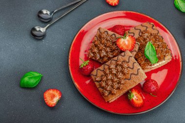 Taze çilekli lezzetli çikolatalı kekler. Tatlı tatlı, günaydın konsepti. Ev yapımı pişirme, krema, sos. Koyu taş zemin, üst görünüm