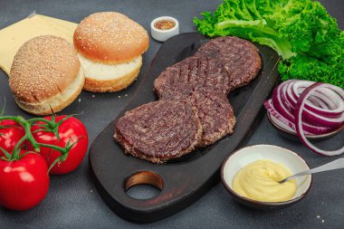 Izgara burger köftesi. Biftek, çörek, sebze ve sos. Ev yapımı Amerikan klasiği, geleneksel piknik, parti ya da Bağımsızlık Günü yemekleri. Koyu taş beton arka plan, kapat