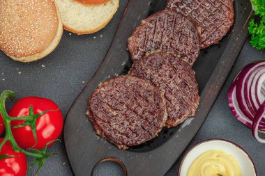 Izgara burger köftesi. Biftek, çörek, sebze ve sos. Ev yapımı Amerikan klasiği, geleneksel piknik, parti ya da Bağımsızlık Günü yemekleri. Koyu taş zemin, üst görünüm