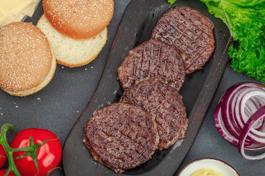 Izgara burger köftesi. Biftek, çörek, sebze ve sos. Ev yapımı Amerikan klasiği, geleneksel piknik, parti ya da Bağımsızlık Günü yemekleri. Koyu taş zemin, üst görünüm