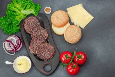 Izgara burger köftesi. Biftek, çörek, sebze ve sos. Ev yapımı Amerikan klasiği, geleneksel piknik, parti ya da Bağımsızlık Günü yemekleri. Koyu taş zemin, üst görünüm