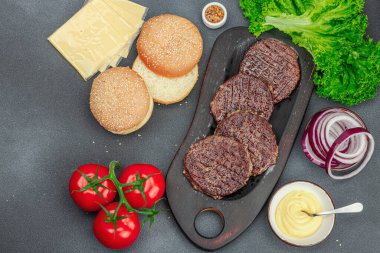Izgara burger köftesi. Biftek, çörek, sebze ve sos. Ev yapımı Amerikan klasiği, geleneksel piknik, parti ya da Bağımsızlık Günü yemekleri. Koyu taş zemin, üst görünüm