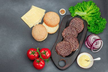 Izgara burger köftesi. Biftek, çörek, sebze ve sos. Ev yapımı Amerikan klasiği, geleneksel piknik, parti ya da Bağımsızlık Günü yemekleri. Koyu taş zemin, üst görünüm