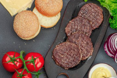Izgara burger köftesi. Biftek, çörek, sebze ve sos. Ev yapımı Amerikan klasiği, geleneksel piknik, parti ya da Bağımsızlık Günü yemekleri. Koyu taş zemin, üst görünüm