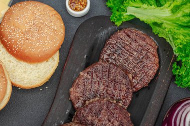Izgara burger köftesi. Biftek, çörek, sebze ve sos. Ev yapımı Amerikan klasiği, geleneksel piknik, parti ya da Bağımsızlık Günü yemekleri. Koyu taş zemin, üst görünüm