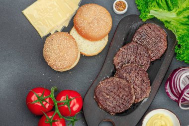 Izgara burger köftesi. Biftek, çörek, sebze ve sos. Ev yapımı Amerikan klasiği, geleneksel piknik, parti ya da Bağımsızlık Günü yemekleri. Koyu taş zemin, üst görünüm
