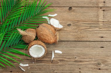 Hindistan cevizi ve palmiye yapraklarıyla yaz tropik arka plan. Geleneksel dekor, desenli meyve, yolculuk konsepti. Eski tahta zemin, düz yatış, üst manzara