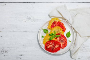 Renkli aile yadigarı domates hasadı. Taze fesleğen yapraklarıyla olgunlaşmış sebzeler. Yaz salatası için sulu malzeme, tahta kaplama arka plan, üst manzara.