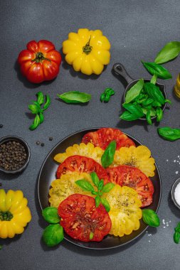 Renkli aile yadigarı domates hasadı. Taze fesleğen yapraklarıyla olgunlaşmış sebzeler. Yaz salatası, baharat ve yağ için sulu malzeme. Sert ışık, karanlık gölge, siyah taş arka plan, üst görüş