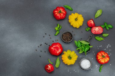 Renkli aile yadigarı domates hasadı. Taze fesleğen yapraklarıyla olgunlaşmış sebzeler. Yaz salatası ve baharatları için sulu malzeme. Siyah taş zemin, düz zemin, üst manzara