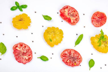 Beyaz arka planda izole edilmiş renkli aile yadigarı domates hasadı. Taze fesleğen yapraklarıyla olgunlaşmış sebzeler. Yaz salatası ve baharatları için sulu malzeme, düz döşeme, kopyalama alanı