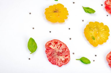 Beyaz arka planda izole edilmiş renkli aile yadigarı domates hasadı. Taze fesleğen yapraklarıyla olgunlaşmış sebzeler. Yaz salatası ve baharatları için sulu malzeme, düz yatak, üst görünüm