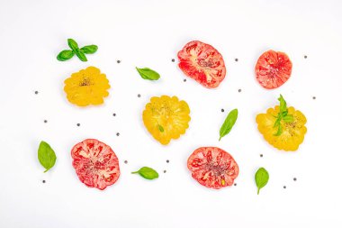 Beyaz arka planda izole edilmiş renkli aile yadigarı domates hasadı. Taze fesleğen yapraklarıyla olgunlaşmış sebzeler. Yaz salatası ve baharatları için sulu malzeme, düz yatak, üst görünüm