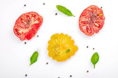 Beyaz arka planda izole edilmiş renkli aile yadigarı domates hasadı. Taze fesleğen yapraklarıyla olgunlaşmış sebzeler. Yaz salatası ve baharatları için sulu malzeme, düz yatak, üst görünüm