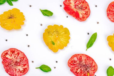 Beyaz arka planda izole edilmiş renkli aile yadigarı domates hasadı. Taze fesleğen yapraklarıyla olgunlaşmış sebzeler. Yaz salatası ve baharatları için sulu malzeme, düz yatak, üst görünüm