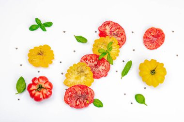 Beyaz arka planda izole edilmiş renkli aile yadigarı domates hasadı. Taze fesleğen yapraklarıyla olgunlaşmış sebzeler. Yaz salatası ve baharatları için sulu malzeme, düz yatak, üst görünüm