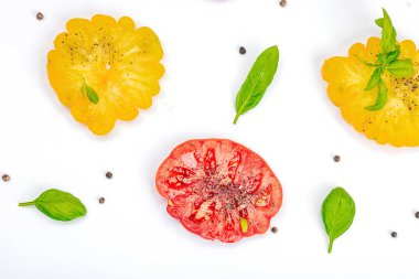 Beyaz arka planda izole edilmiş renkli aile yadigarı domates hasadı. Taze fesleğen yapraklarıyla olgunlaşmış sebzeler. Yaz salatası ve baharatları için sulu malzeme, düz yatak, üst görünüm