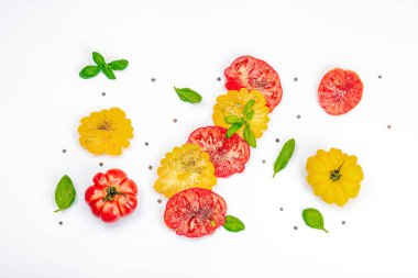 Beyaz arka planda izole edilmiş renkli aile yadigarı domates hasadı. Taze fesleğen yapraklarıyla olgunlaşmış sebzeler. Yaz salatası ve baharatları için sulu malzeme, düz yatak, üst görünüm