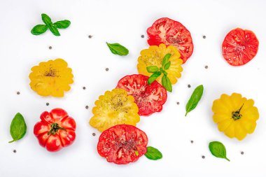 Beyaz arka planda izole edilmiş renkli aile yadigarı domates hasadı. Taze fesleğen yapraklarıyla olgunlaşmış sebzeler. Yaz salatası ve baharatları için sulu malzeme, düz yatak, üst görünüm