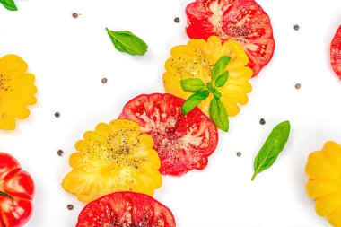 Beyaz arka planda izole edilmiş renkli aile yadigarı domates hasadı. Taze fesleğen yapraklarıyla olgunlaşmış sebzeler. Yaz salatası ve baharatları için sulu malzeme, düz yatak, üst görünüm