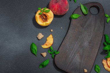 Meyve aşçılığı geçmişi. Olgun şeftali, esmer şeker ve taze fesleğen yaprağı. Tahta kesme tahtası, sert ışık, karanlık gölge.