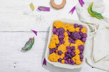 Karnabahar, sarı ve mor, pişirmeye hazır. Sağlıklı yiyecekler, baharatlar, zeytinyağı. Sert ışık, karanlık gölge, beyaz ahşap zemin, üst manzara