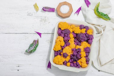 Karnabahar, sarı ve mor, pişirmeye hazır. Sağlıklı yiyecekler, baharatlar, zeytinyağı. Sert ışık, karanlık gölge, beyaz ahşap zemin, üst manzara