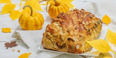 Balkabağı tohumlu taze ekmek. Ev yapımı konsept. Sonbahar dekoru, balkabağım, sonbahar yaprakları. Sert ışık, koyu gölge, beyaz ahşap arkaplan, afiş biçimi