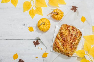 Balkabağı tohumlu taze ekmek. Ev yapımı konsept. Sonbahar dekoru, balkabağım, sonbahar yaprakları. Sert ışık, karanlık gölge, beyaz ahşap zemin, üst manzara