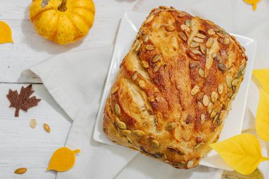 Balkabağı tohumlu taze ekmek. Ev yapımı konsept. Sonbahar dekoru, balkabağım, sonbahar yaprakları. Sert ışık, karanlık gölge, beyaz ahşap zemin, üst manzara