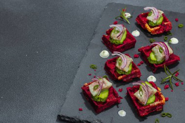 Lezzetli bir iştah açıcı. Baharatlı ve soslu pancar gözlemelerinin üzerinde ringa balığı var. Modaya uygun sert ışık, karanlık gölge, siyah taş beton zemin, kopyalama alanı