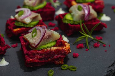 Lezzetli bir iştah açıcı. Baharatlı ve soslu pancar gözlemelerinin üzerinde ringa balığı var. Modaya uygun sert ışık, karanlık gölge, siyah taş beton arka plan, kapat