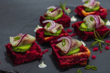 Lezzetli bir iştah açıcı. Baharatlı ve soslu pancar gözlemelerinin üzerinde ringa balığı var. Modaya uygun sert ışık, karanlık gölge, siyah taş beton arka plan, kapat