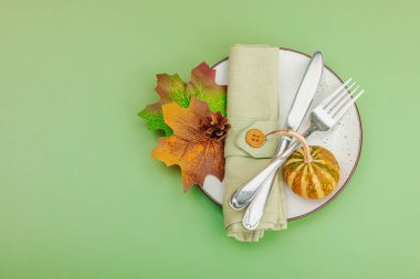 Sonbahar sofrası. Şükran Günü çatal bıçak takımı, geleneksel sonbahar dekorasyonu, düz yatış. Neşeli bir ortam, balkabağı, yapraklar, Savannah Green arka plan, üst manzara.