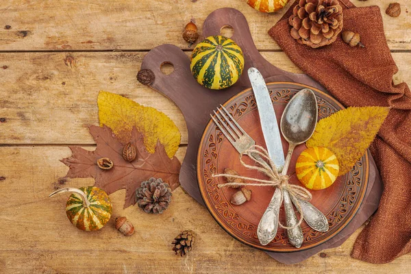 Autumn table setting. Thanksgiving cutlery, traditional fall decor, flat lay. Festive cozy mood, rustic style. Pumpkin, leaves, wooden background, top view