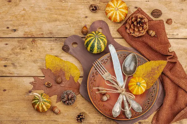 Autumn table setting. Thanksgiving cutlery, traditional fall decor, flat lay. Festive cozy mood, rustic style. Pumpkin, leaves, wooden background, top view