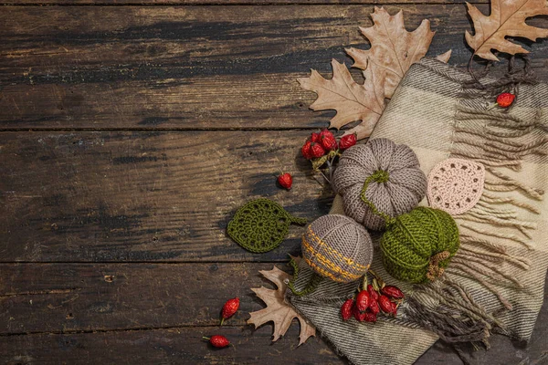Autumn cozy mood composition. Crocheted pumpkins, handmade, fall hobby concept. Props and traditional decoration, knitting.Hard light, dark shadow, old wooden background, top view
