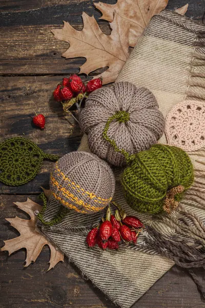 Autumn cozy mood composition. Crocheted pumpkins, handmade, fall hobby concept. Props and traditional decoration, knitting.Hard light, dark shadow, old wooden background, top view