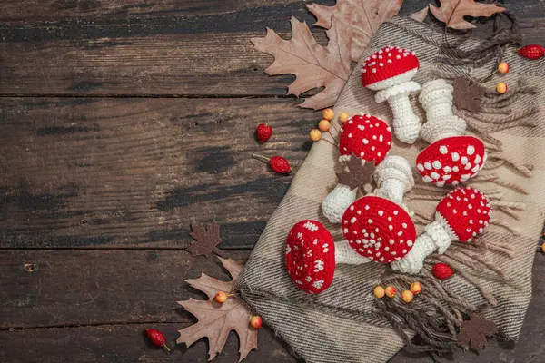 Autumn cozy mood composition. Crocheted amanita mushroom, handmade, fall hobby concept. Props and traditional decoration, knitting. Hard light, dark shadow, old wooden background, top view