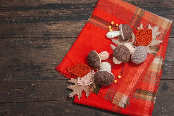 Autumn cozy mood composition. Crocheted mushroom, handmade, fall hobby concept. Props and traditional decoration, knitting. Hard light, dark shadow, old wooden background, top view
