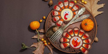 Autumn table setting. Thanksgiving cutlery, traditional fall decor, flat lay. Festive cozy mood, handmade crocheted turkeys and leaves, brown background, banner format clipart