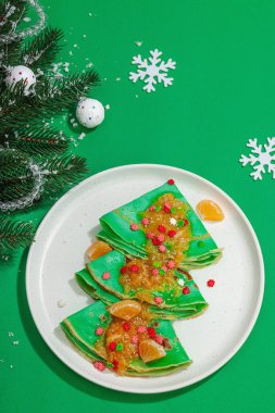 Mandalina soslu ve tatlı serpilmiş Noel gözlemeleri. Yeni yıl ziyafeti tatlısı, yemek için hazır. Yeşil arkaplan, geleneksel dekor, düz yatak, üst görünüm