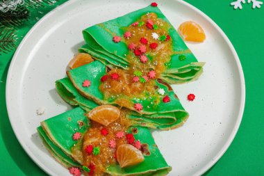 Mandalina soslu ve tatlı serpilmiş Noel gözlemeleri. Yeni yıl ziyafeti tatlısı, yemek için hazır. Yeşil arkaplan, geleneksel dekor, düz yatak, yakın çekim